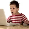 12 Year Olds — Young boy sitting at a laptop in a casual, neutral pose ready for text overlay.