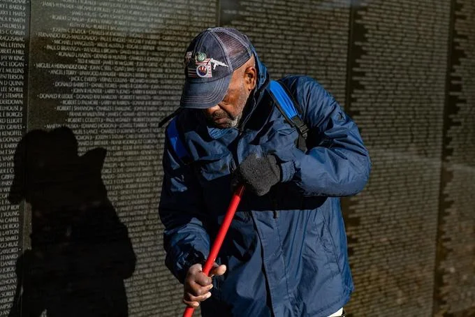 2018 2019 United States Government Shutdown — Volunteer in blue jacket cleaning the black granite Vietnam Veterans Memorial wall