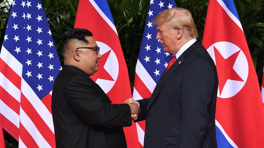 2018 North Korea United States Summit — Donald Trump and Kim Jong-un shaking hands in front of US and North Korean flags