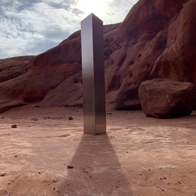 2020 Metal Monoliths — Metal monolith standing prominently in a desert canyon surrounded by rust-colored rock formations.