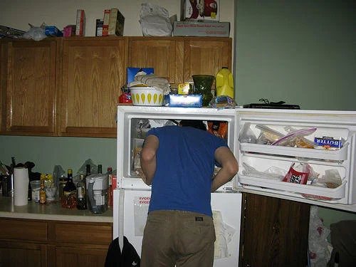 241543903 Heads In Freezers — Photograph of a person from behind leaning into a kitchen refrigerator with head in freezer.