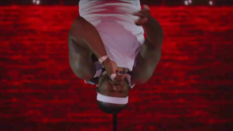 50 Cent hanging upside down during Super Bowl LVI halftime in white pants against red background.