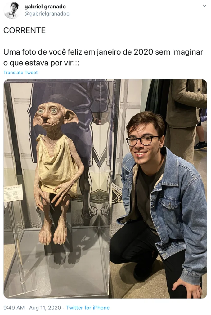 A Photo Of You In January 2020 Without Imagining What Would Come — Tweet screenshot of a smiling young man kneeling next to a Dobby the House Elf display