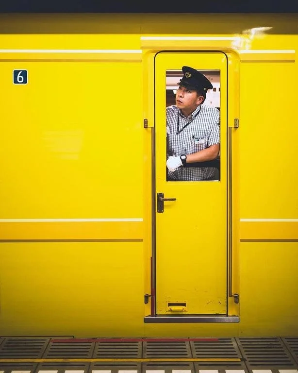 Accidental Wes Anderson — Train conductor leaning from a yellow train car doorway