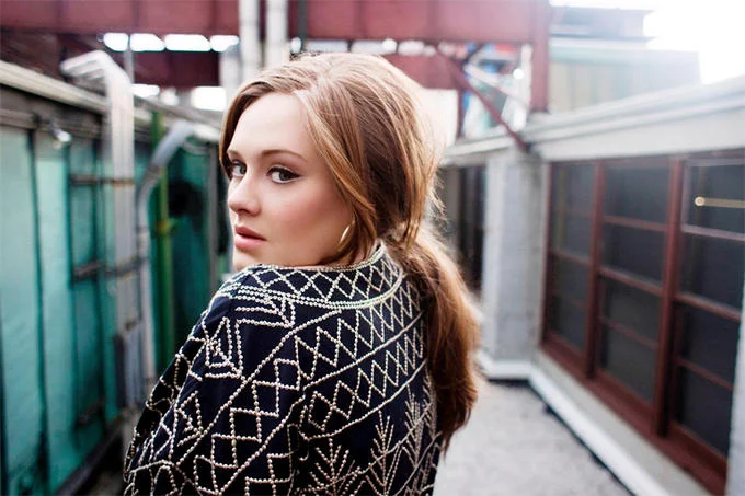 Adele looking over her shoulder in a patterned jacket outdoors