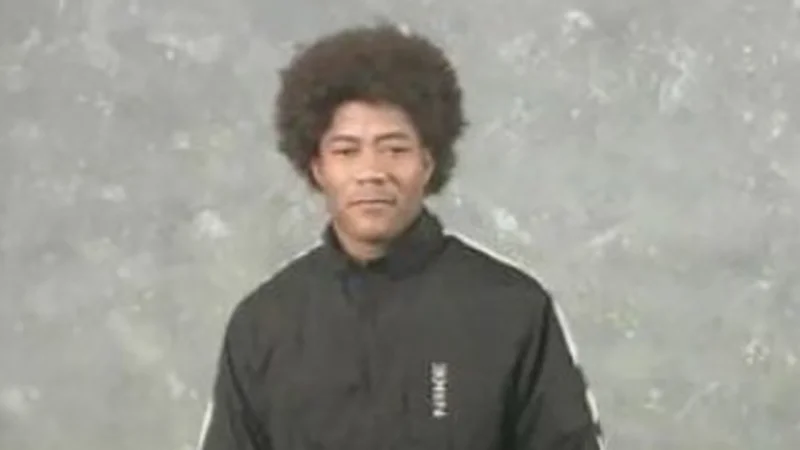 Man with afro hairstyle in black jacket standing against grey backdrop from Afro Ninja video