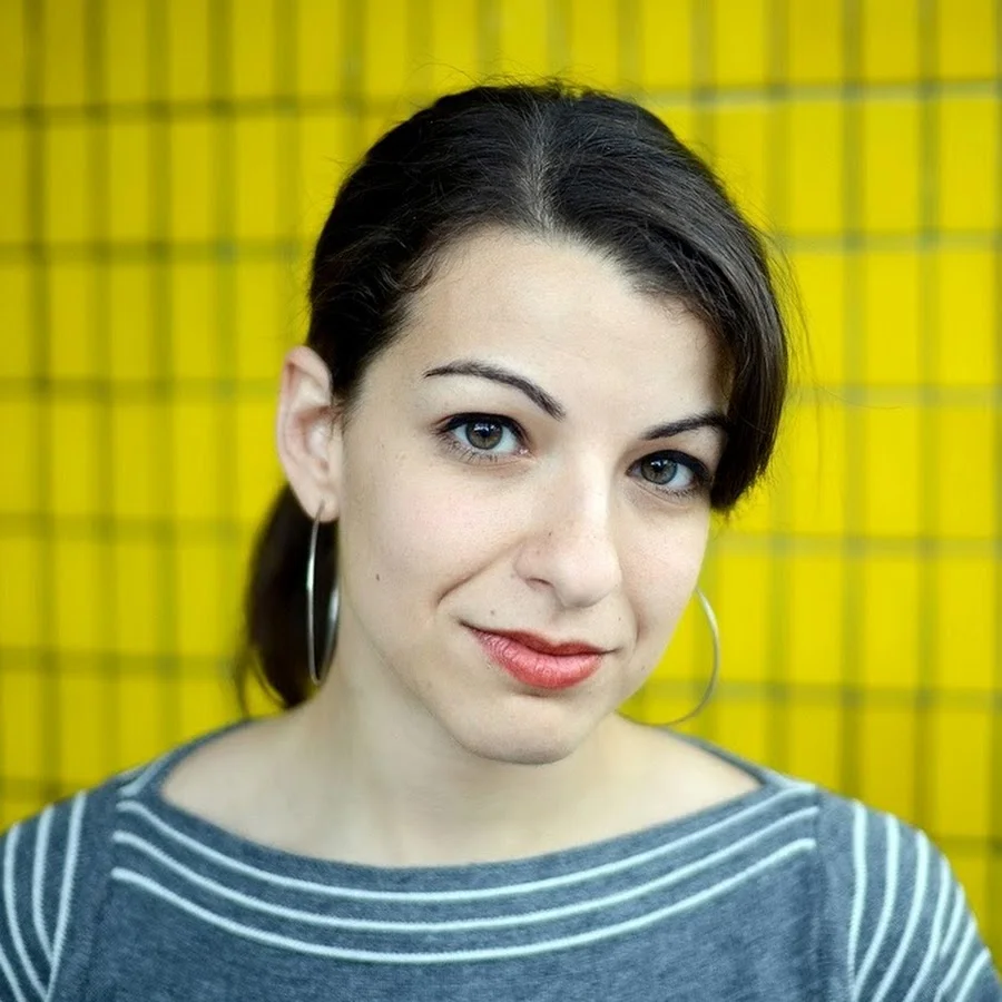 Portrait of Anita Sarkeesian in front of a yellow tiled wall