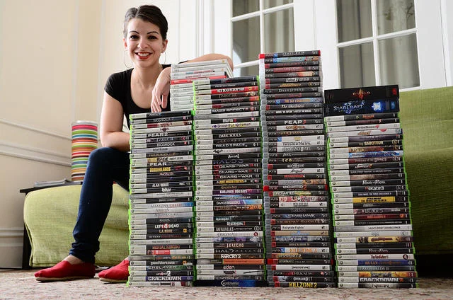 Anita Sarkeesian posing next to large stacks of video games