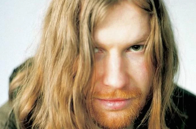 Close-up portrait of Richard D. James, aka Aphex Twin, with long hair and red beard
