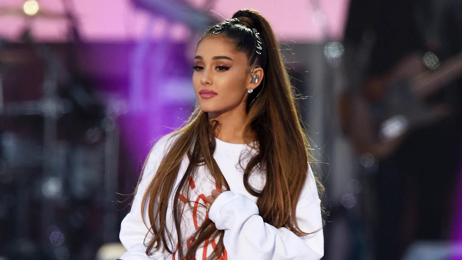 Ariana Grande performing on stage with signature high ponytail and white sweatshirt