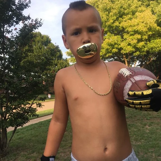 Baby Gronk — Young athlete in confident pose with gold accessories and football in athletic gloves.