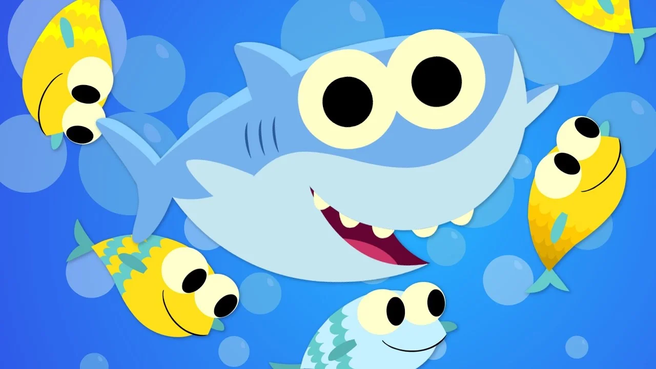 Colorful animated Baby Shark character with large round eyes, wide smile, surrounded by fish and bubbles.