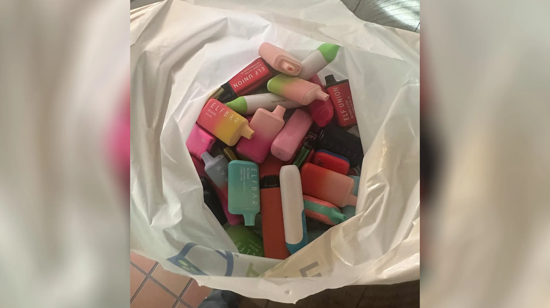Bag Full of Elf Bars — White plastic bag filled with colorful Elf Bar disposable vapes on a tiled floor