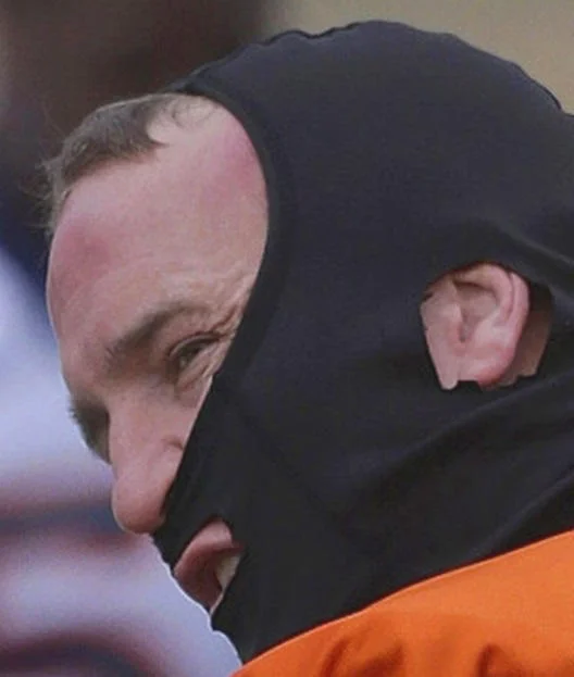 Bait And Switch Videos Pictures — Close-up of a balding man wearing a black ski mask and orange jumpsuit.