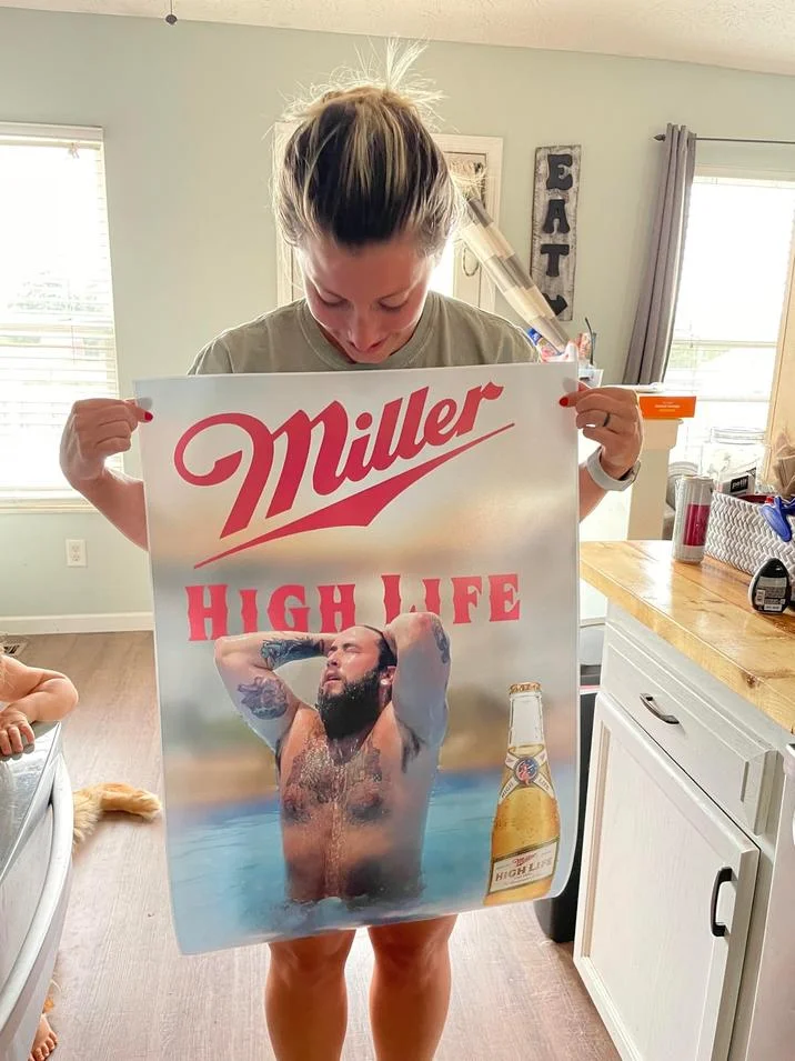 Beer Poster Trend — Woman holding a printed Miller High Life beer poster in her kitchen