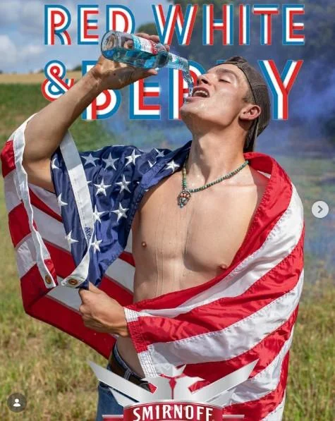 Beer Poster Trend — Shirtless man wrapped in an American flag drinks Smirnoff Red White and Berry in a field