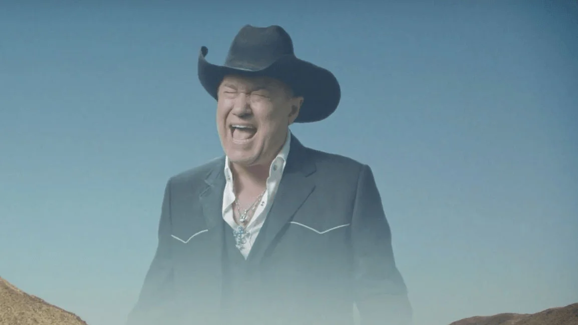 Screaming cowboy Jimmy Barnes in black hat wailing against a desert sky from the Big Enough music video
