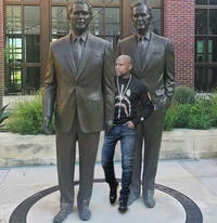 Bill Clinton Between Two Bushes Photograph — A photograph of a young man standing between the two bronze statues of George H.W. Bush and George W. Bush at the