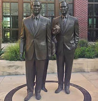 Bill Clinton Between Two Bushes Photograph — A clear photograph of Bill Clinton grinning and peering out between two large bronze statues of George H.W. Bush