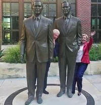 Bill Clinton Between Two Bushes Photograph — A photograph at the Bush Presidential Library showing a woman in a red top with arms outstretched in front of the