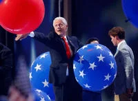 Bill Clinton Loves Balloons — Bill Clinton reaches out with both arms toward a large red balloon on the 2016 DNC stage, with giant blue star-decorated balloons