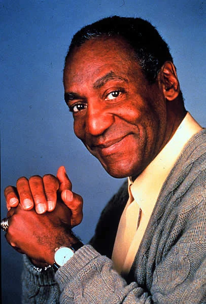 Portrait of Bill Cosby smiling in a gray cardigan sweater