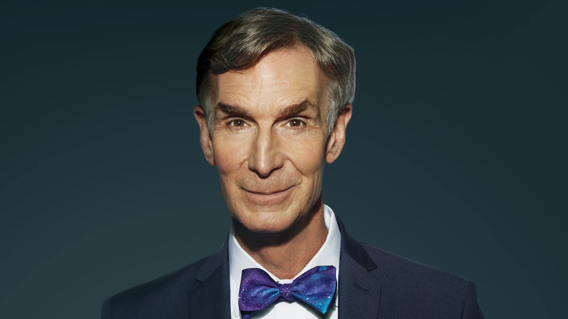 Bill Nye smiling in a dark suit with a galaxy-print bow tie