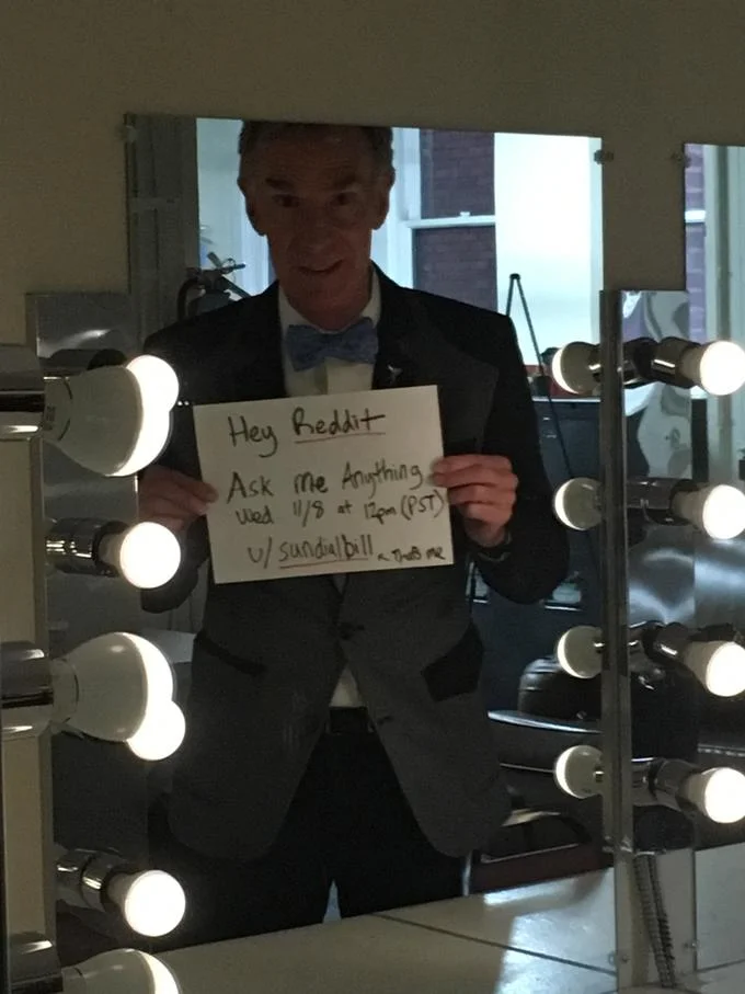 Bill Nye holding a handwritten sign announcing a Reddit AMA