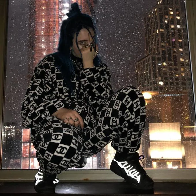 Billie Eilish crouched by window in Chanel checkered outfit