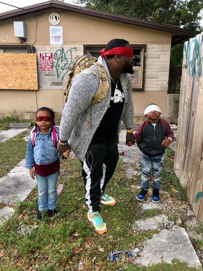 Bird Box Challenge — Blindfolded man walks with two small blindfolded children outside a house