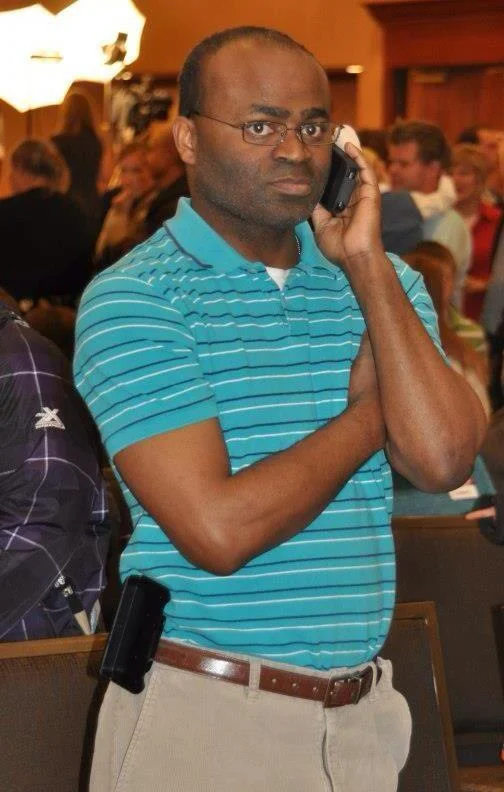 Black Guy On The Phone — Full-body photo of bald Black man with glasses in teal striped polo holding phone to ear with skeptical look