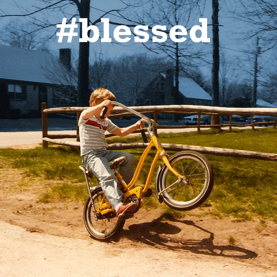 Young boy popping a wheelie on a yellow bike with '#blessed' hashtag text overlay