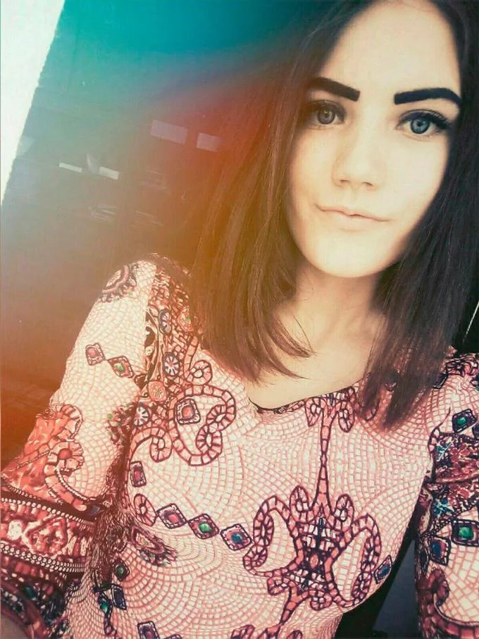 Blue Whale Challenge — A selfie-style portrait of a young woman with dark brown hair, bold brows, and striking green eyes, wearing an ornate patterned lace top