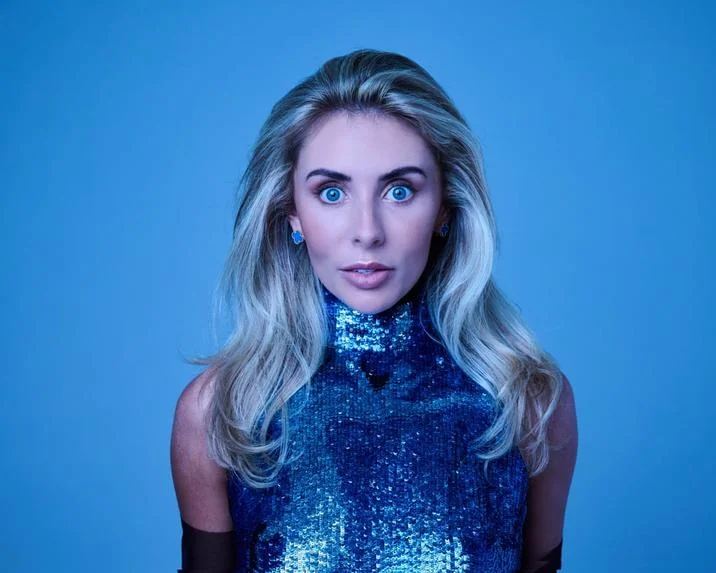 Bonnie Blue Staring — Close cropped portrait of Bonnie Blue with wide blue eyes in a blue sequined top against a blue backdrop