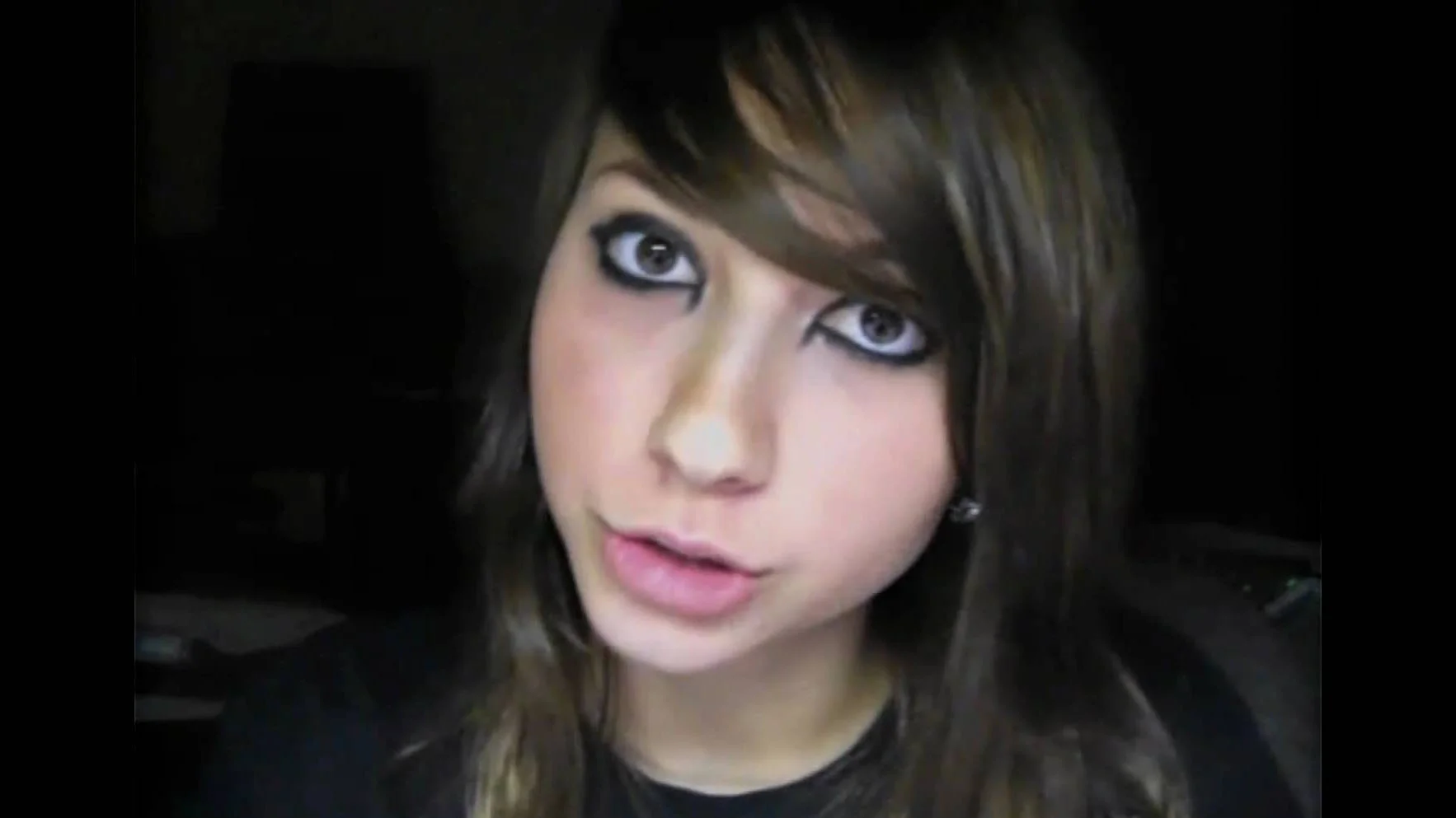 Close-up webcam still of Boxxy with heavy black eyeliner and side-swept bangs staring into the camera