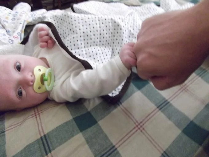 Bro Fist — Adult fist bumping the tiny fist of a baby lying on a blanket