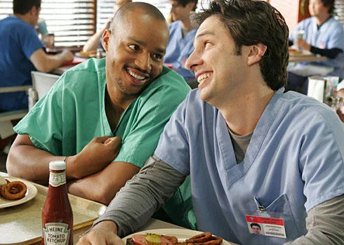 Bro — Production photograph from Scrubs showing Donald Faison and Zach Braff in hospital scrubs laughing and leaning on each other at diner table.