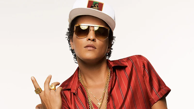 Bruno Mars in white cap, gold sunglasses, and red striped shirt with gold chains.