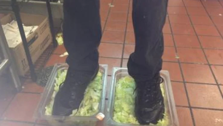 Burger King Foot Lettuce — Person in black work boots standing in two plastic bins of shredded lettuce on a red-tiled fast food kitchen floor