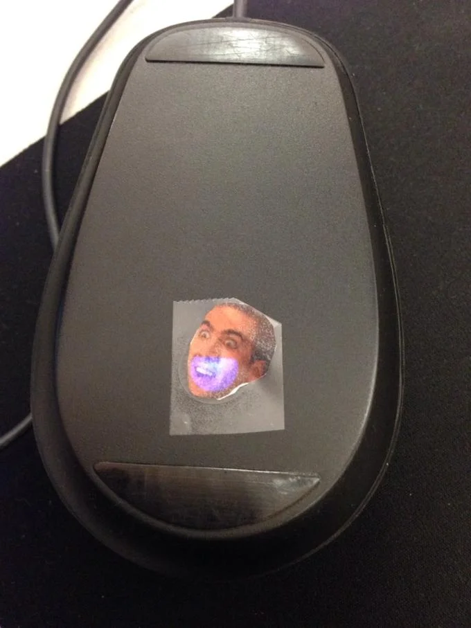 Caging — Computer mouse with a Nicolas Cage face sticker on top