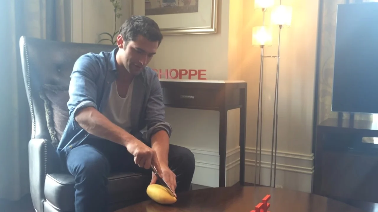 Can I Get Another Mango — Man seated in leather chair cutting a yellow mango on a wooden table with a knife