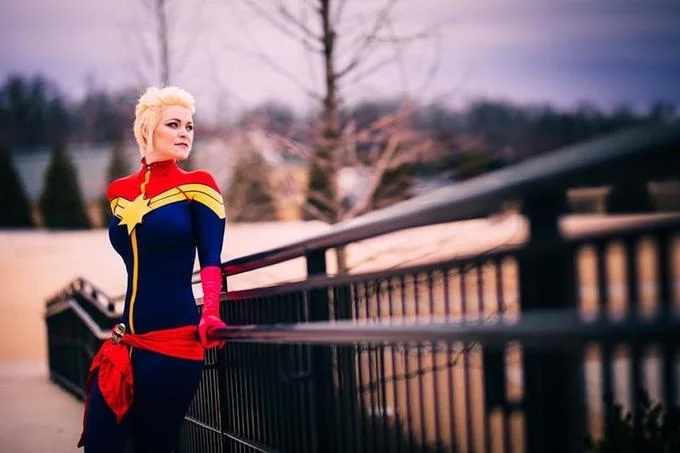Captain Marvel cosplayer with mohawk hair posing outdoors by a railing