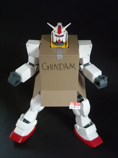 Gundam action figure wearing tiny cardboard box GUNDAM parody