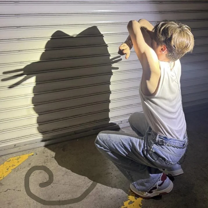 Cat Shadow Trend — A light-haired person crouches near a garage shutter creating a large clear cat shadow on the wall.