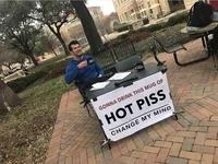 Cropped image of Steven Crowder at table with sign reading HOT PISS CHANGE MY MIND.