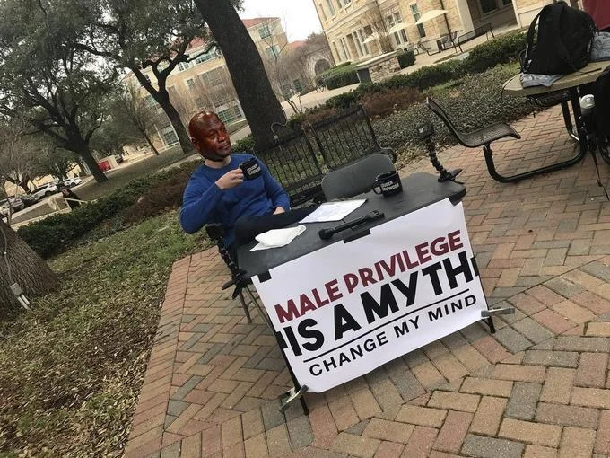 Steven Crowder with sign displaying MALE PRIVILEGE IS A MYTH in red and CHANGE MY MIND.