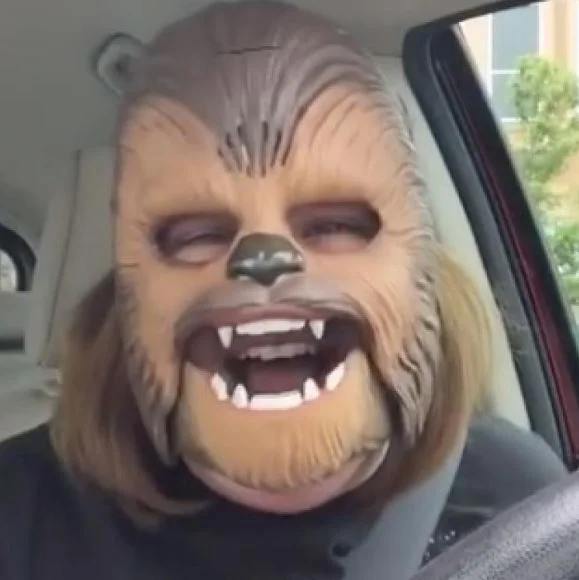 Chewbacca Mom — Person wearing a Chewbacca mask with open mouth showing teeth, sitting in a car