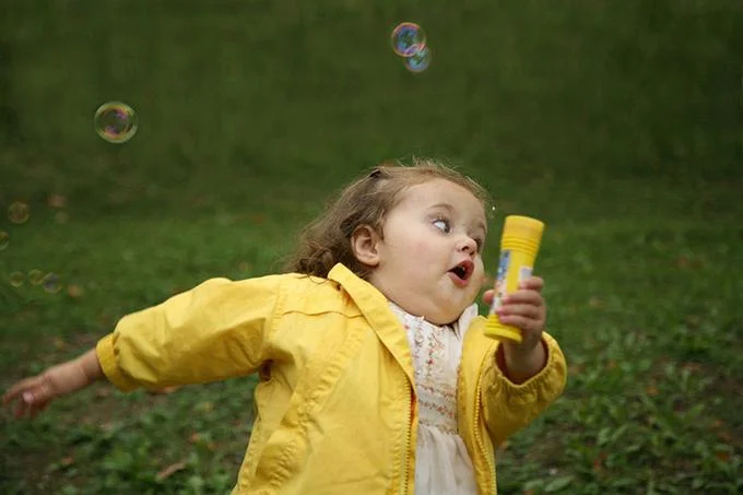 Chubby Bubbles Girl — Original photo of young girl in yellow jacket chasing bubbles on a grassy lawn