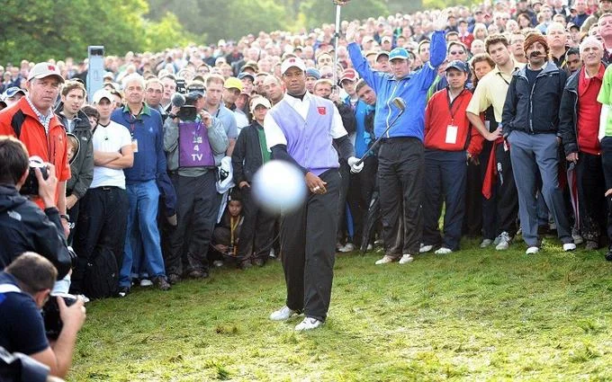 Tiger Woods hitting a golf ball toward the camera at the 2010 Ryder Cup with Cigar Guy in the crowd