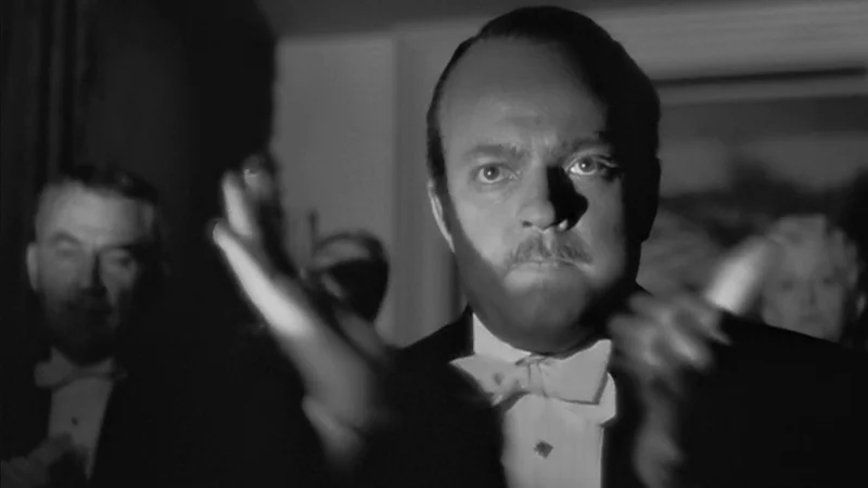 Citizen Kane Clapping — Orson Welles as Charles Foster Kane clapping in tuxedo, black-and-white film still.